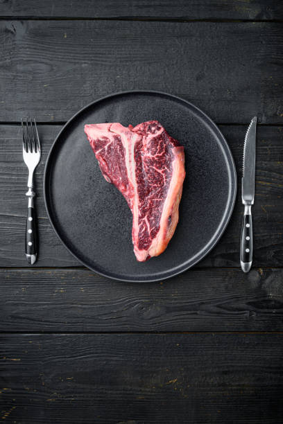 raw fresh dry aged beef t-bone steak, on plate, on black wooden table background, top view flat lay, with copy space for text - veal t bone steak raw steak imagens e fotografias de stock