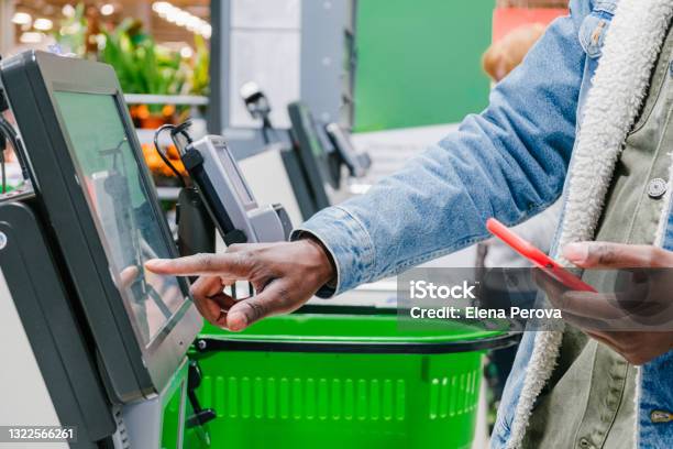 The Finger Of An African Man In Closeup At The Supermarket Checkout Selects The Desired Product On The Electronic Screen Of The Cash Register With A Phone In His Hands Stock Photo - Download Image Now