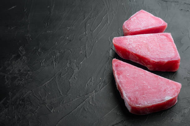 istock Raw frozen tuna fish fillet, on black stone background , with copyspace  and space for text 1322567887