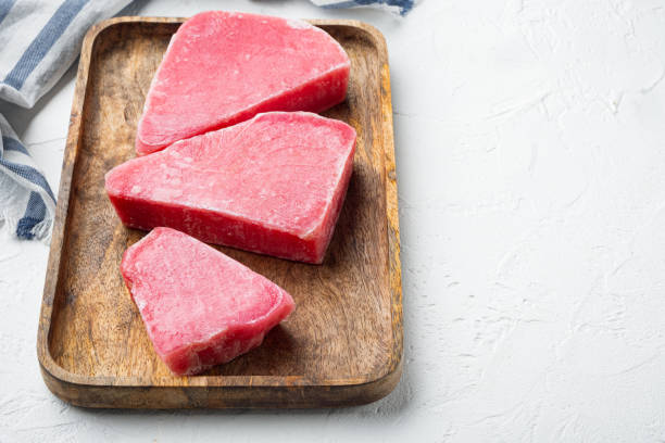 istock Frozen tuna fish steaks, on wooden tray, on white stone  background , with copyspace  and space for text 1322568928