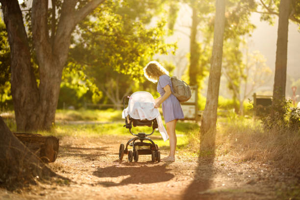 Mother cover her little baby in a stroller with a blanket while out for a walking on a sunny summer afternoon