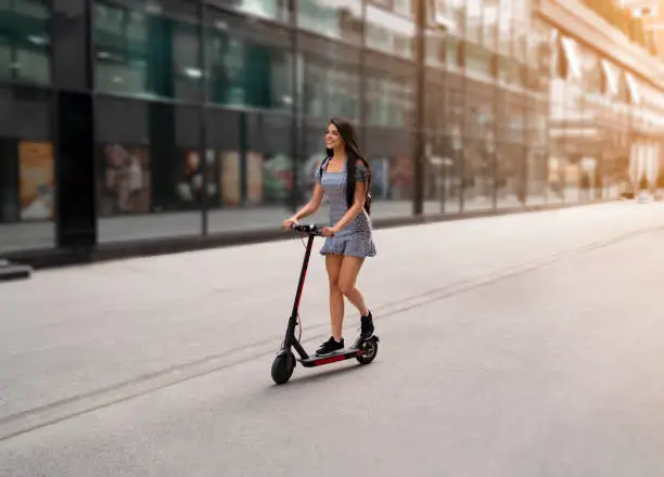 Photo of Amazing dark hair girl cruising through the city on e scooter