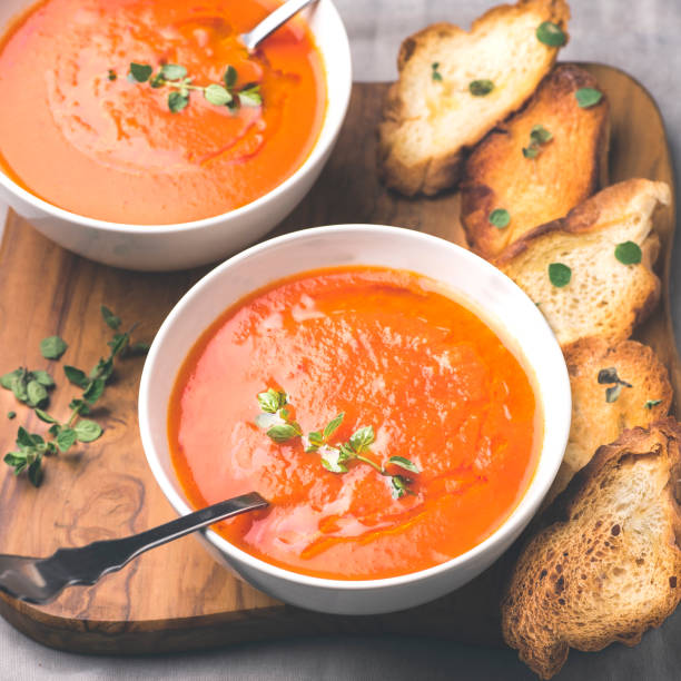 토마토 수프는 올리브 나무 트레이와 회색 면 배경에 흰색 그릇에 크루통과 허브와 함께 제공됩니다. 건강한 식품 개념, 사각 작물 - tomato soup red basil table 뉴스 사진 이미지