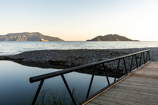 Container ship with a wooden bridge over the river, island and seascape in Fethiye, Turkey.