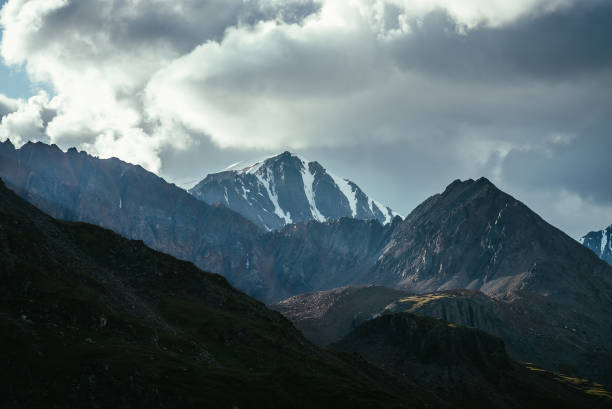 istock Atmospheric mountain landscape with silhouettes of rocks and snowbound sharp pinnacle under cloudy sky. Great rocks with snow. Beautiful mountain scenery with snow peaked top. Snow-capped pointy peak. 1322585741