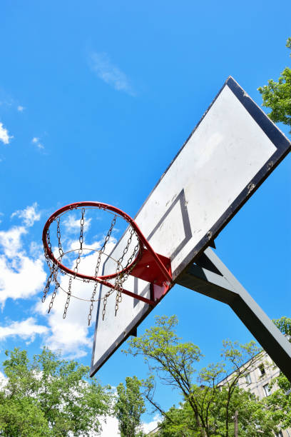 istock Basketball hoop and backboard against a bright blue sky with white clouds. Shot from below 1322589141