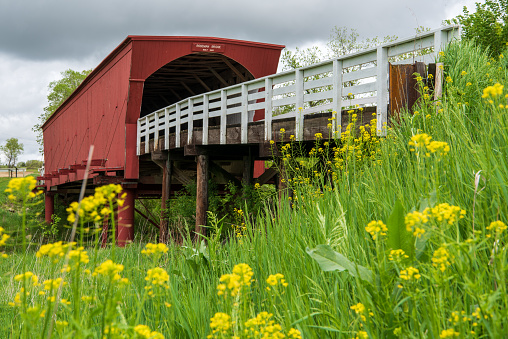 Roseman Covered Bridge, Winterset, Madison County, Iowa.\nBuilt in 1883 by Harvey P. Jones and George K. Foster, Roseman is 107 feet in length and sits in its original location. It was renovated in 1992 at a cost of $152,515. In Robert James Waller’s novel, The Bridges of Madison County, and the movie of the same name, Roseman is the bridge Robert Kincaid seeks when he stops at Francesca Johnson’s home for directions. It is also where Francesca leaves her note inviting him to dinner.\nAlso known as the “haunted” bridge, Roseman is where two sheriff’s posses trapped a county jail escapee in 1892. It is said the man rose up straight through the roof of the bridge, uttering a wild cry, and disappeared. He was never found, and it was decided that anyone capable of such a feat must be innocent.