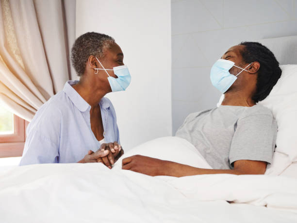 colpo di una donna anziana mascherata che si prende cura del marito malato a letto a casa - cold and flu flu virus bed couple foto e immagini stock