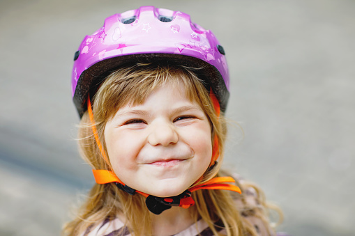 Portrait of happy smiling preschool girl with bycicle helmet on head. Cute toddler child. Safe bike driving with children concept. Safety helmet for kids.