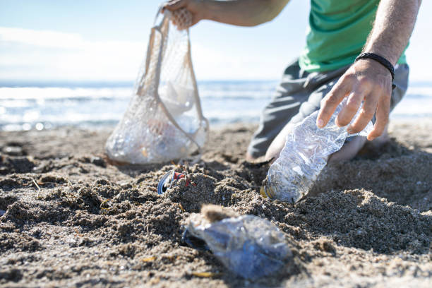 istock Man hand picked plastic bottle waste on beach. mesh bag. Man cleaning the beach from plastic.Selective focus 1322612558