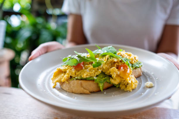 istock a woman holding and eating scrambled eggs and avocado open sandwich 1322614268