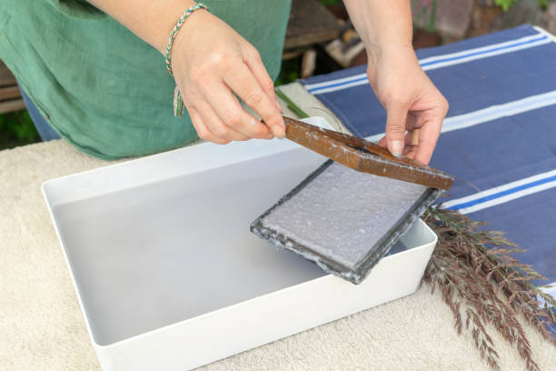 istock Woman holding frame for making paper sheets from waste paper pulp. Selective focus. Decorative and applied art. Recycling concept, ecology. 1322615292