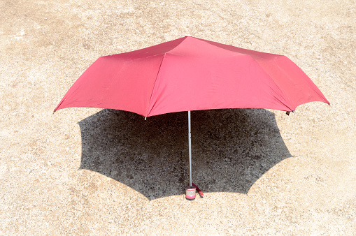 UV umbrella in the summer sun. Red color beach umbrella blocking the sunlight. Shadow on the sandy floor. Sunbath tanning shade shadow background.