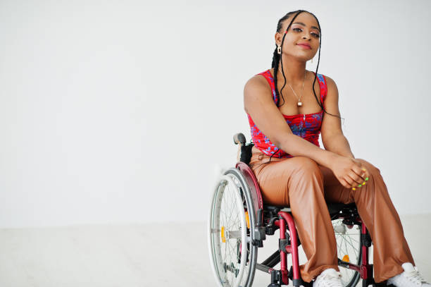 Young disabled African American woman Young disabled African American woman in wheelchair against white wall. wheelchair stock pictures, royalty-free photos & images
