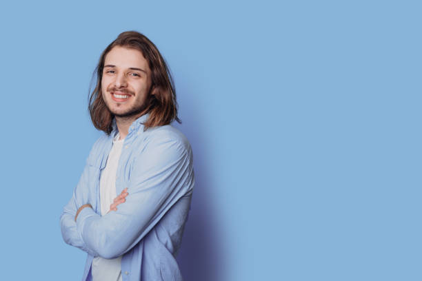 istock Caucasian man with beard is smiling at camera on a blue studio wall with free space posing with crossed hands 1322623780