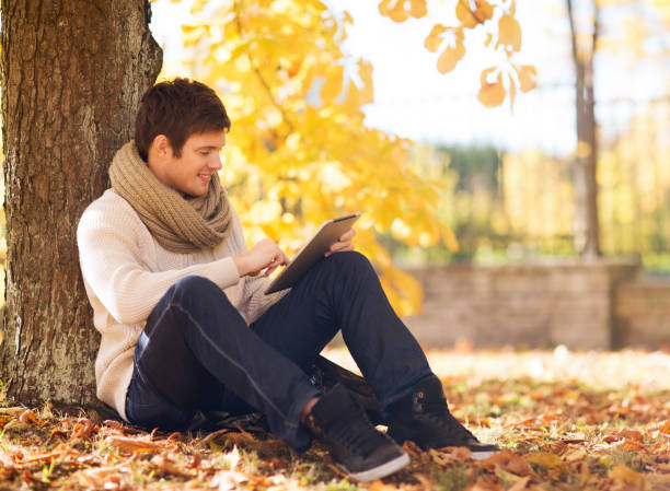 istock smiling young man with tablet pc in autumn park 1322624781
