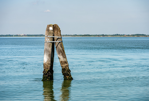 Venice lagoon with three big wooden poles implanted in the seabed called Briccola or Bricola (Dolphin), used to indicate the viable routes in the sea to boats. Veneto, Italy, Europe.