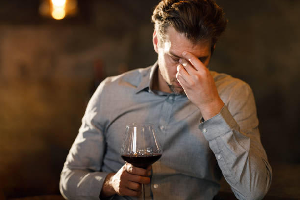 hombre de negocios que tiene un dolor de cabeza mientras bebe vino tinto en un bar. - exhaustion tired men after work fotograf�ías e imágenes de stock