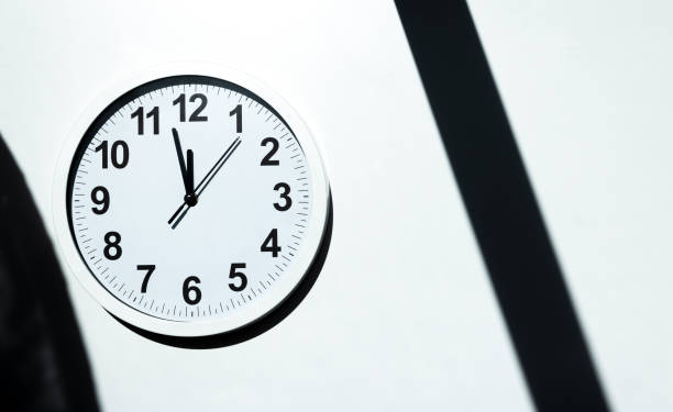 Close up to a wall clock, with five minutes to twelve o'clock