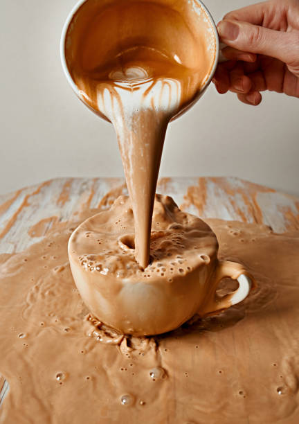 le cappuccino déborde de la tasse. le café se déverse de la tasse sur la table avec des éclaboussures. сoffee éclaboussures sur le bord - overflowing photos et images de collection