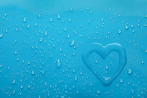 Heart shape of water and drops on light blue background, top view