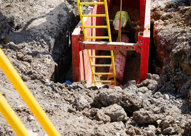 Photo of groundworker installing clay drainage pipe while in the trench supported by trench box