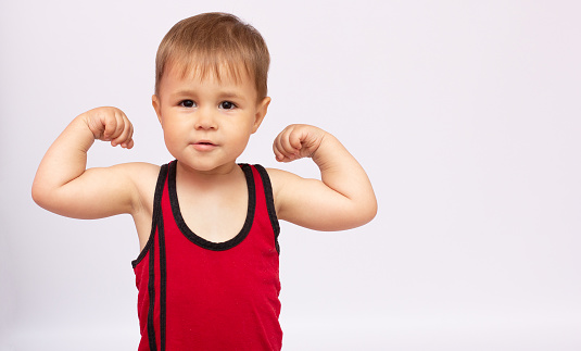 little strong boy showing his biceps, gray background copy space