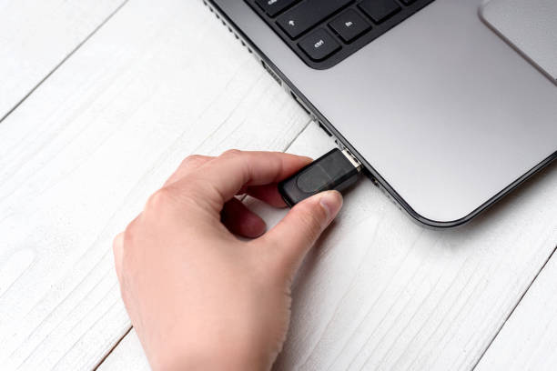 istock Hand inserting USB flash drive into laptop computer on white background. Close up of woman hand plugging pendrive on laptop at home. Copying data from flash drive to laptop computer 1322643314