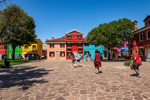 Burano, Italy - June 2th, 2021: Burano island with beautiful multi colored houses and a group of tourist visiting the village in a sunny spring day with clear sky. Venetian lagoon, Venice, UNESCO world heritage site, Veneto, Italy, Europe.