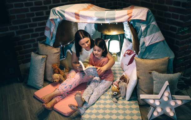 istock Mother and daughter reading a book in a diy tent 1322646094