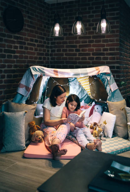 Mother and daughter having a pajama party reading a book Mother and daughter having a pajama party reading a book in a diy tent slumber party stock pictures, royalty-free photos & images