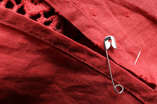 Metal safety pin on red fabric, closeup