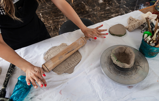 Ceramic artist shaping clay with a lace sample after flattening clay mud with a rolling pin.