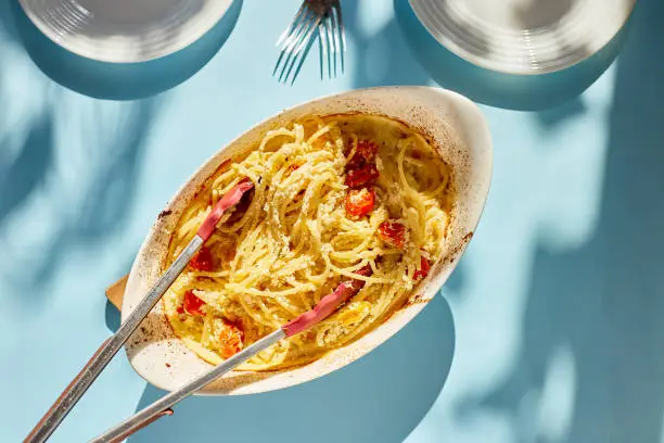 Photo of Trending viral recipe of baked tomatoes and feta with pasta on a blue background sunlight