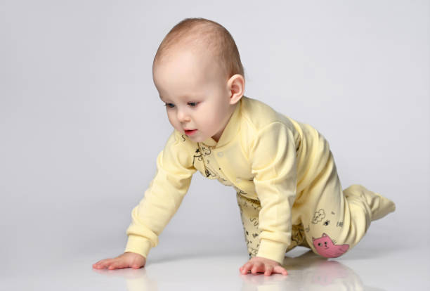 istock Curious Toddler infant kid crawling on a gray studio background, he dressed with yellow children's cotton overalls with a cat 1322660963