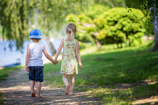 Sweet toddler kids, walking together hand in hand on a little path next to a lake with boats