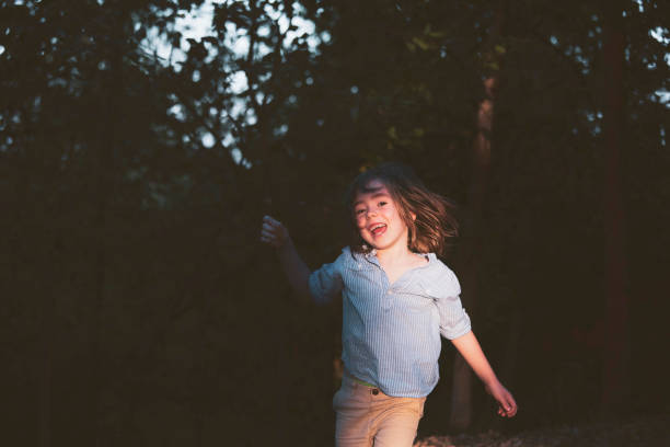 Happy little boy enjoys the setting sun in the forest. Running and jumping on sunset. Relaxing in nature. Low key lighting portrait.