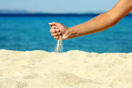 female hand pours sand on the seashore