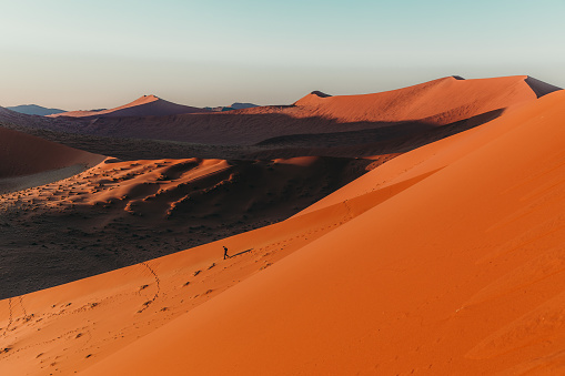 Young man exploring the scenic desert landscape with dunes during bright sunset in Namib-Naukluft National Park