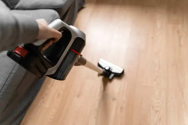 Photo of Cleaning wooden floor with wireless vacuum cleaner. Handheld cordless cleaner. Household appliance. Housework modern equipment