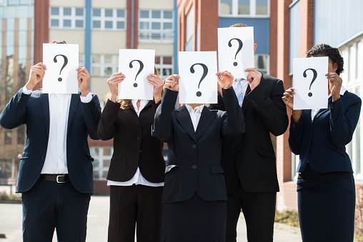 Group Of Businesspeople Hiding Face Behind Question Mark Sign;Outdoor