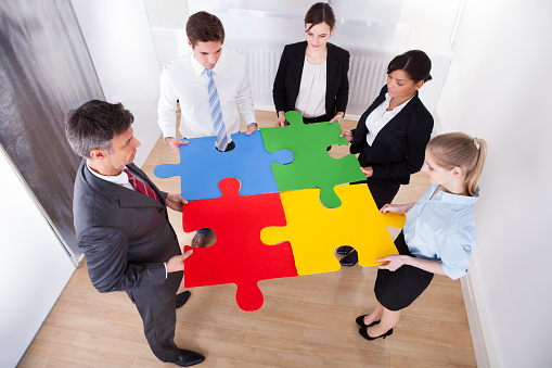 High Angle View Of Businesspeople Holding Multi Coloured Jigsaw Puzzle