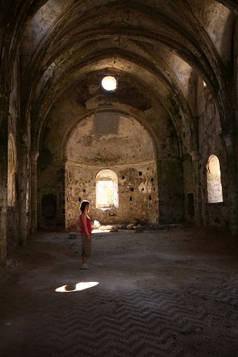 Muğla, Turkey-April 26, 2013: Architectural details from inside the ruins of the monastery in the ghost village of Kayaköy, abandoned many years ago. Young tourist woman examines the walls.