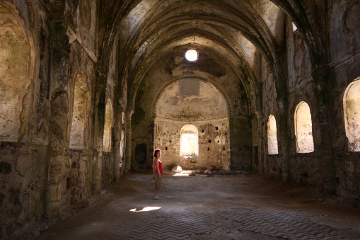 Muğla, Turkey-April 26, 2013: Architectural details from inside the ruins of the monastery in the ghost village of Kayaköy, abandoned many years ago. Young tourist woman examines the walls.