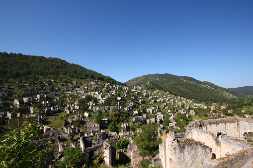Muğla, Turkey-April 26, 2013: Stone house ruins in the ghost village of Kayaköy, abandoned many years ago. The houses have no roofs and trees have grown inside them.