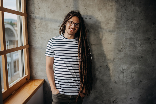 Smiling man with dreadlocks posing for a shot in front of concrete wall