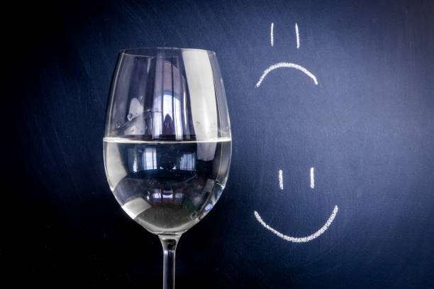 Half-full or half-empty glass of water, with an happy face and unhappy face, showing optimism or pessimism, concept stock photo