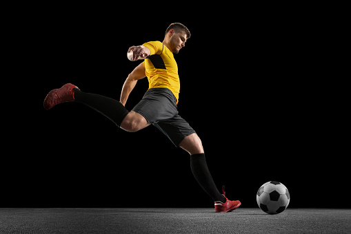 Powerful, flying and running above the field. Young football soccer player in action, motion isolated on black studio background. Concept of sport, movement, energy and dynamic, healthy lifestyle.