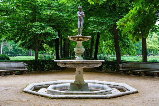 White stone fountain with statue in public park with green vegetation.