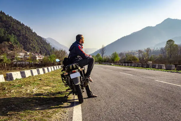 man sitting at motorcycle at tarmac road with beautiful natural view at morning image is taken at shergaon arunachal pradesh india.